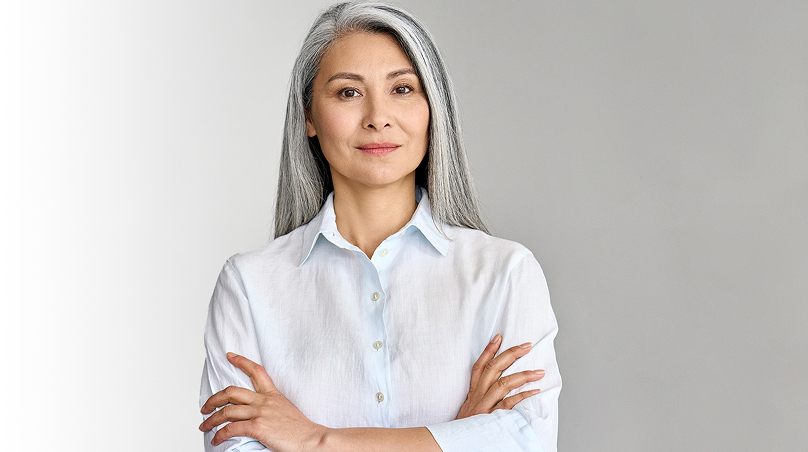 Woman with long silver hair wearing a button-up shirt with her arms folded across her chest